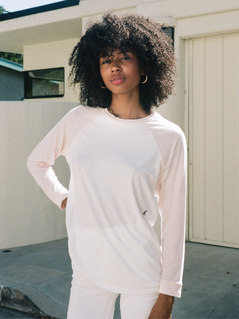 Dark haired woman in loose fitting long sleeved raglan shirt in blush and white